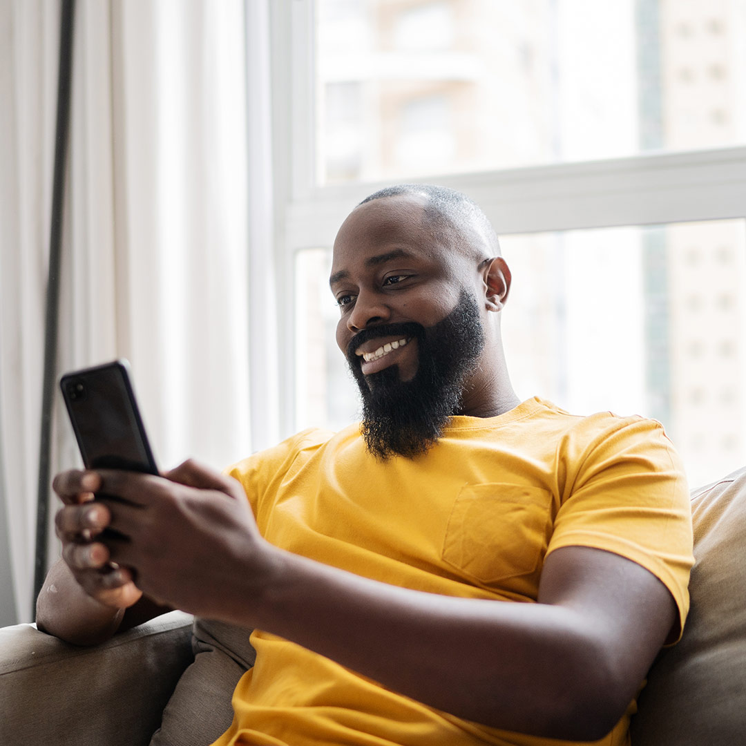 Man sitting on couch in his home reviewing benefits on a mobile device